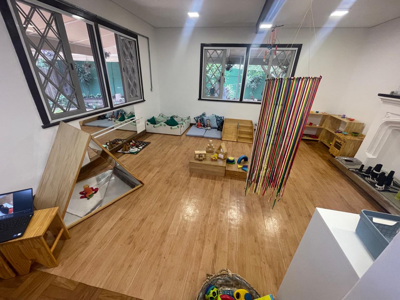 Sala dos bebês com colchonetes, espelho e móbile de fitas coloridas